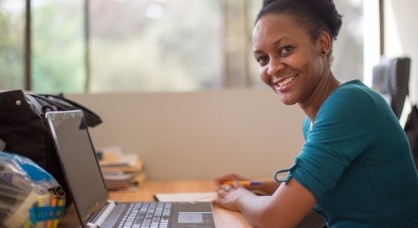 A women looking into the camera. She has a laptop in front of her.