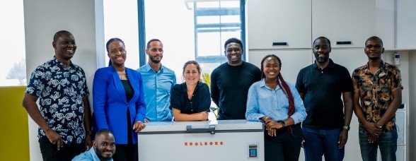 A diverse team of eight professionals posing with a 'KOOLBOKS' freezer in a modern office setting, smiling and looking towards the camera.