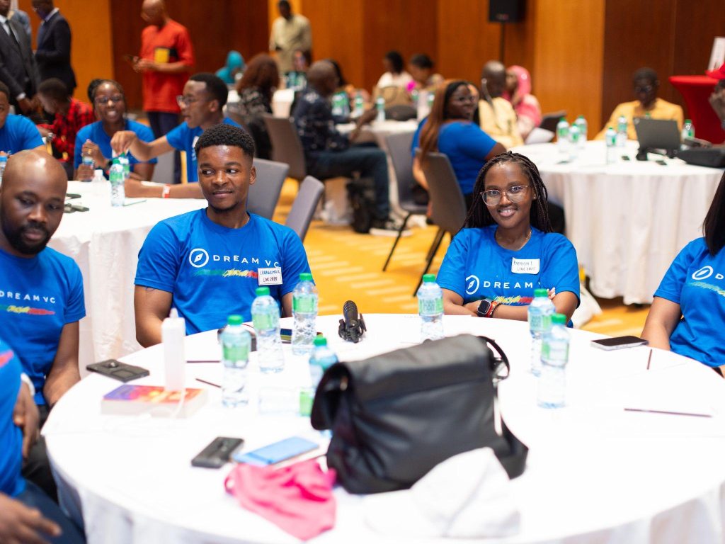 fund-frontendventures-story-context-dreamvc-20260519 - Africa Growth Fund Group of attendees in blue DREAM VC shirts seated around round tables with water bottles and conference materials in a bright event hall.