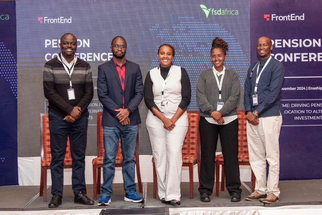 fund-frontendventures-story-context-pension-panel-20260519 - Africa Growth Fund Five professionals pose on a conference stage for a group photo, badges hanging from lanyards, in front of a blue backdrop with conference branding and logos.