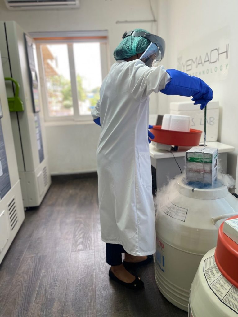 fund-yemaachi-story-lab-20260706 - Africa Growth Fund Lab worker in a white lab coat, face shield, and green cap pours from a cryogenic dewar with nitrogen fog in a lab.
